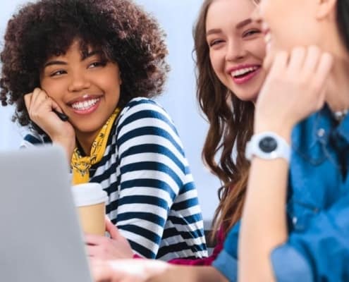 three teenage girls sitting at desk with laptop, smiling about gifts for teenage girls