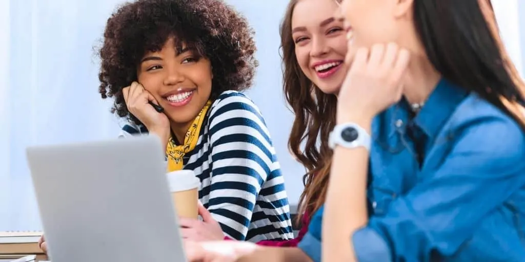 three teenage girls sitting at desk with laptop, smiling about gifts for teenage girls