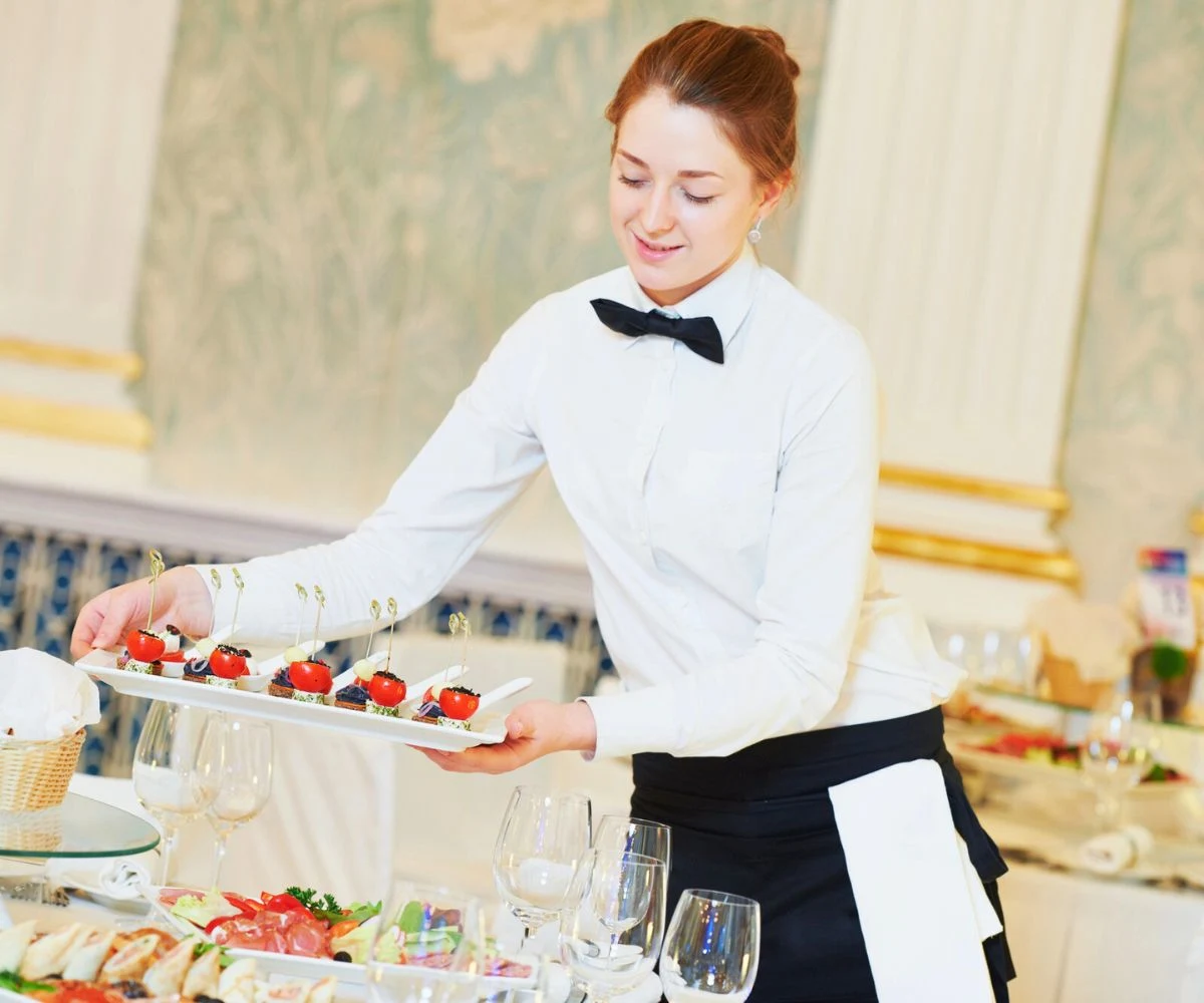 teen girl in catering uniform replacing food on table