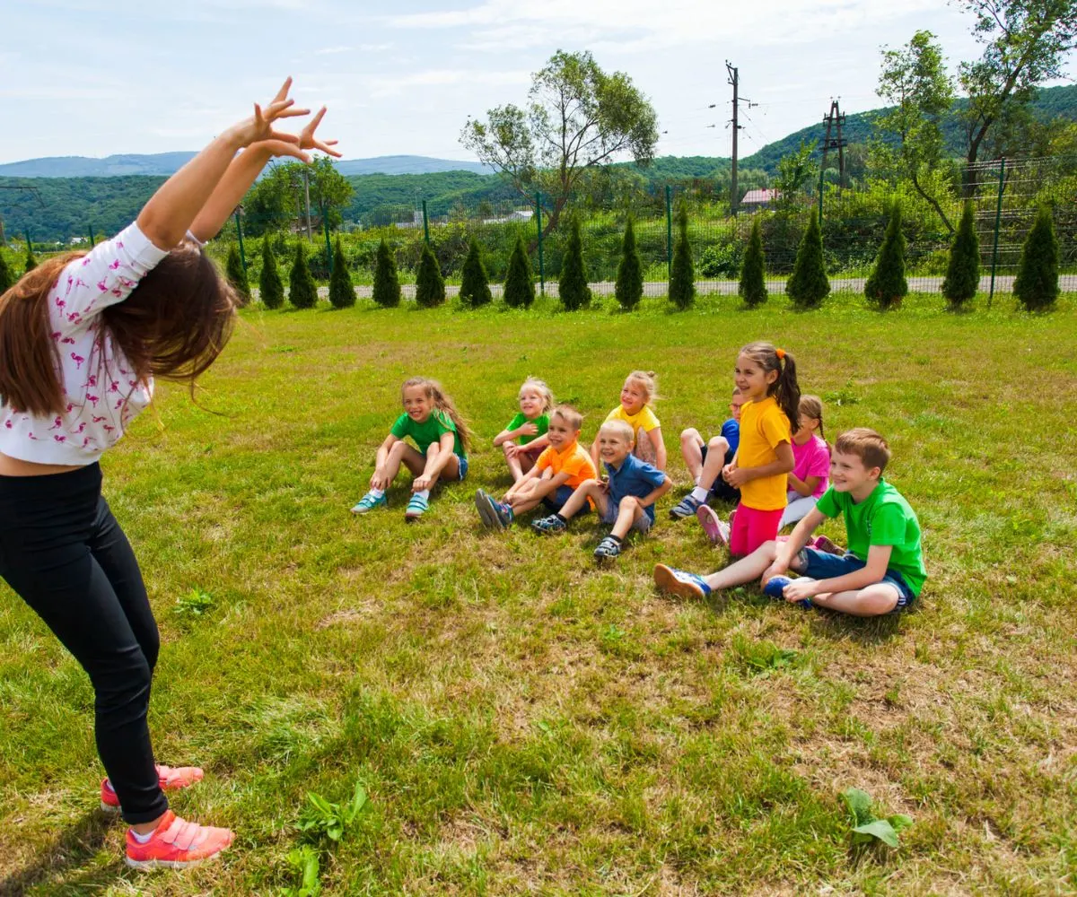 teen girl counselor with group of young kids doing charades