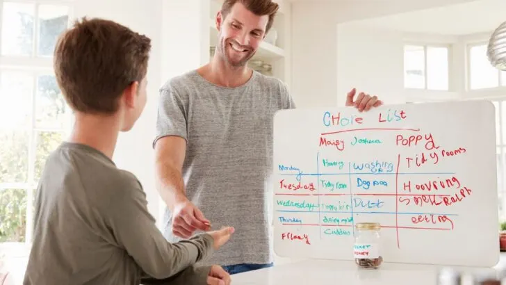 father with chore chart, handing reward to son