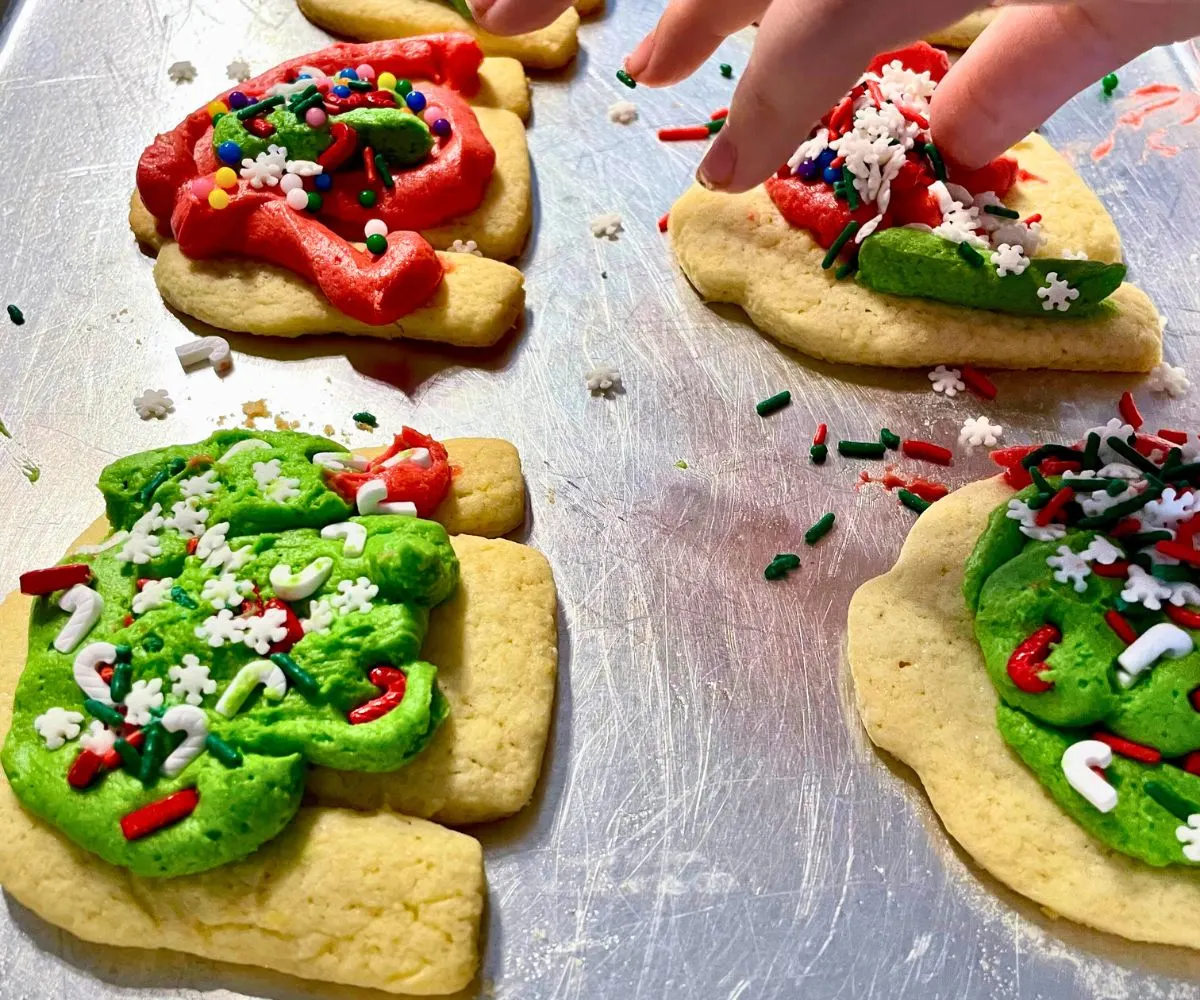 teen decorating a bunch of ugly Christmas sweater cookies on cookie tray
