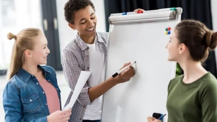 three teen students writing examples of smart goals for students on a large paper pad