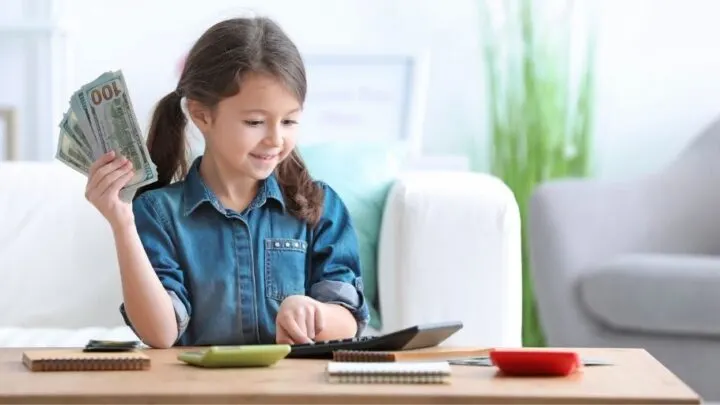 young girl with money in hand, calculator, learning money management for kids