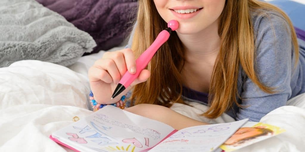 teen student dreaming about her student vision board and writing in journal with pink pen