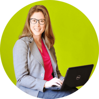 author Amanda L. Grossman on laptop, with green background, wearing glasses and business suit
