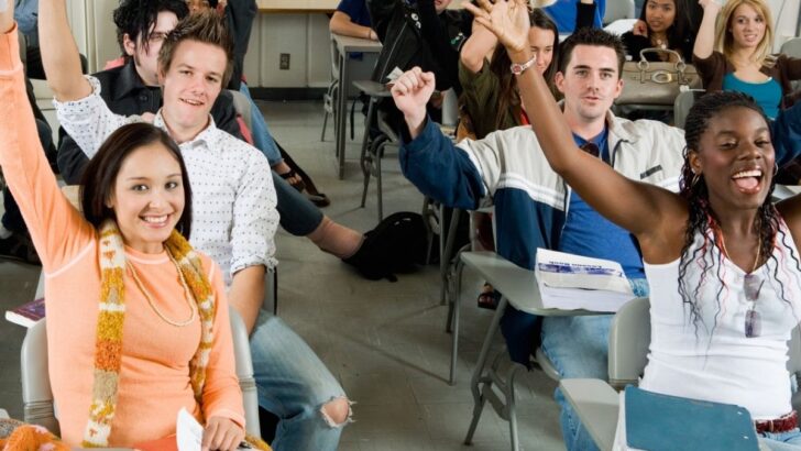 class of teen students raising hands and smiling