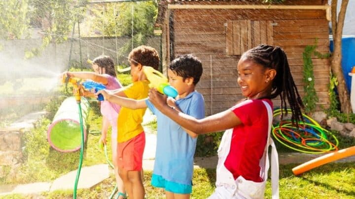 four kids in line having fun with water guns out in backyard