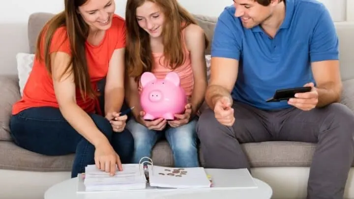 teen girl with piggy bank talking about why she should save money with parents on couch