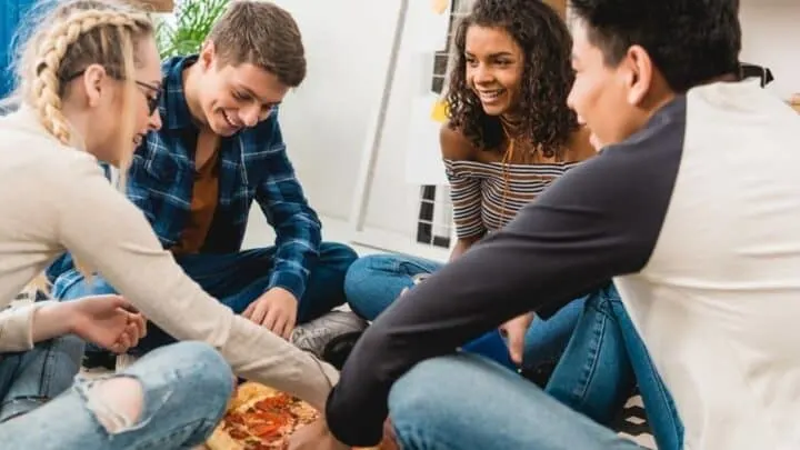 group of teens around a pizza, having a good time