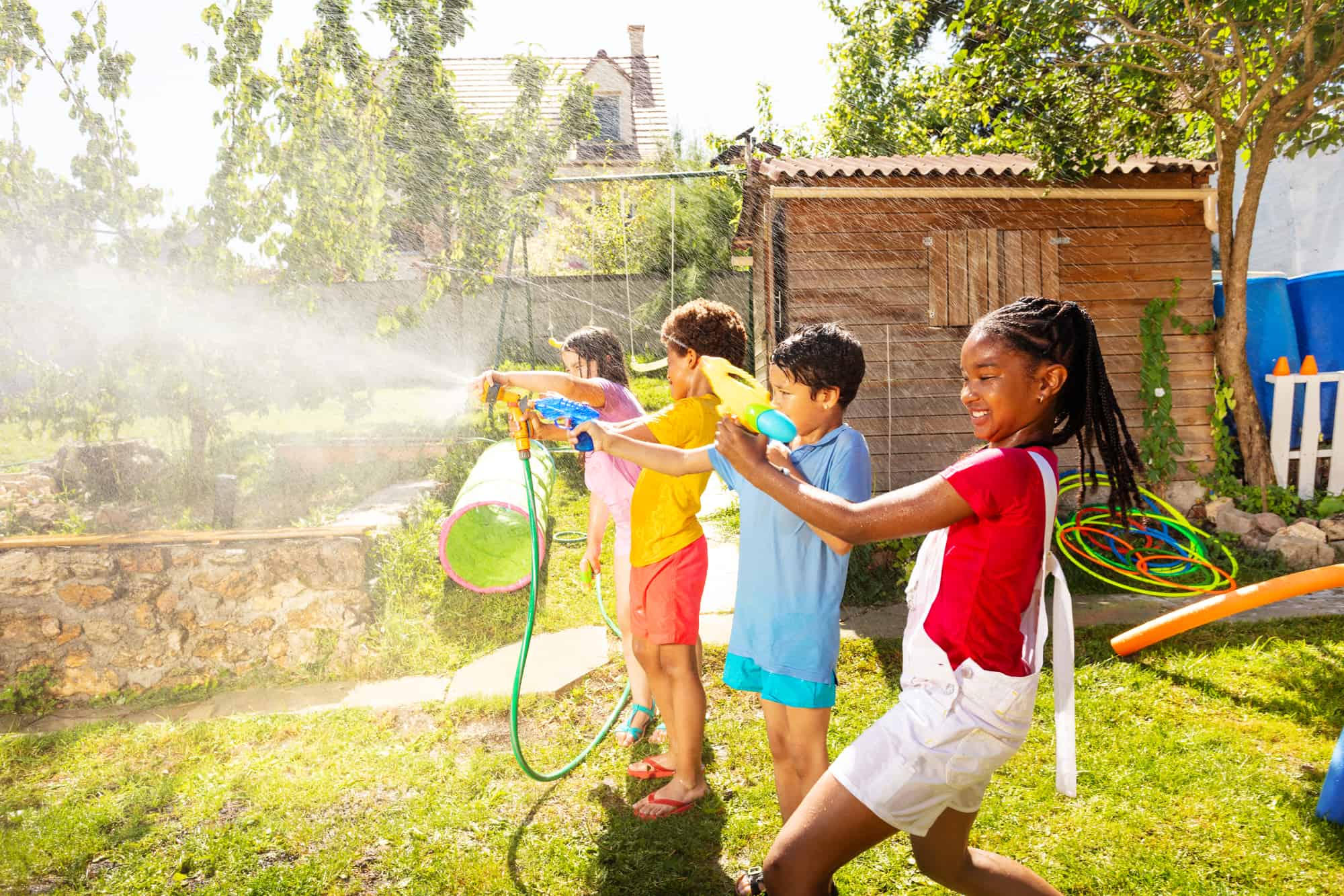 four kids in line having fun with water guns playing backyard activities for kids, outdoors