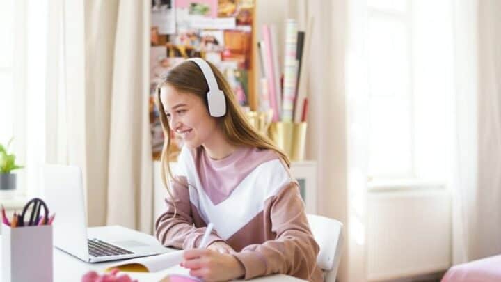 teen girl with headphones on at laptop, smiling at her short term financial goals