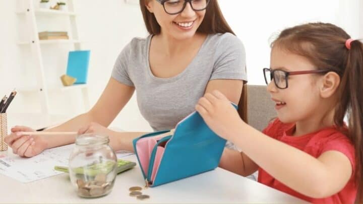 kid putting money into a wallet next to mother, who's using bank worksheet pdfs to teach her banking