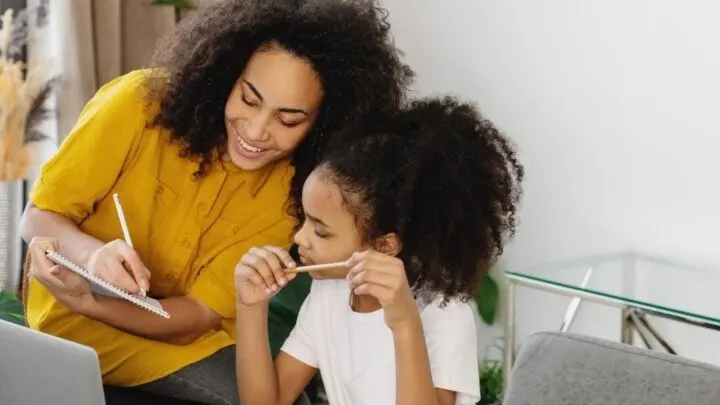 mother with daughter at desk smiling, identifying needs and wants on a worksheet they're working on