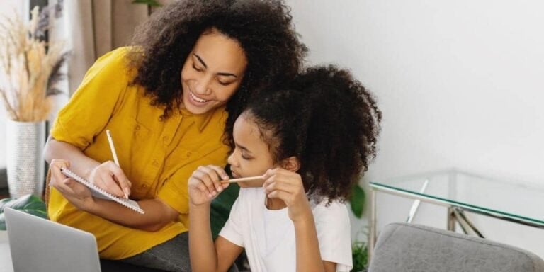 mother with daughter at desk smiling, identifying needs and wants on a worksheet they're working on
