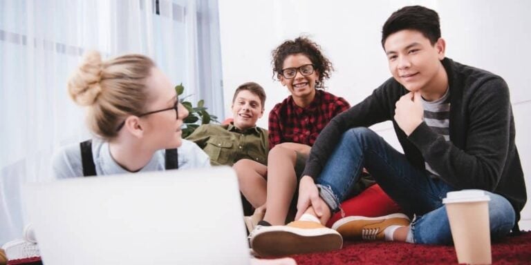 group of teens on ground hanging out, playing a stock market game for kids on laptop