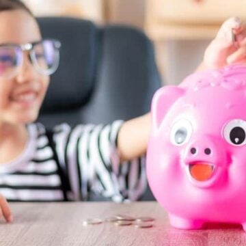girl kid putting allowance for kids money into pink piggy bank