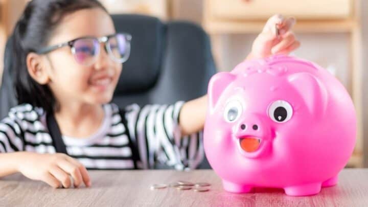 girl kid putting allowance for kids money into pink piggy bank
