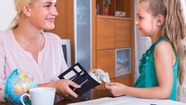 mother with wallet handing appropriate amount of allowance over to young daughter, smiling