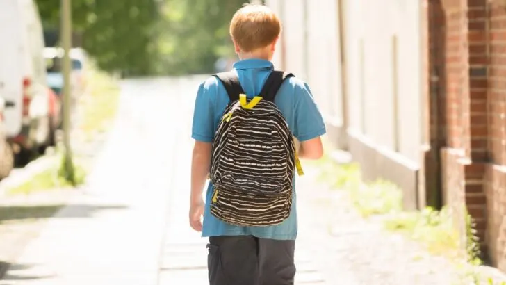 teen boy walking away on sidewalk with backpack
