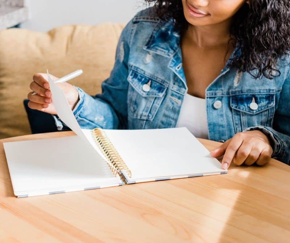 young mother sitting down with journal to figure out her money mission statement and what she wants to teach her child about money