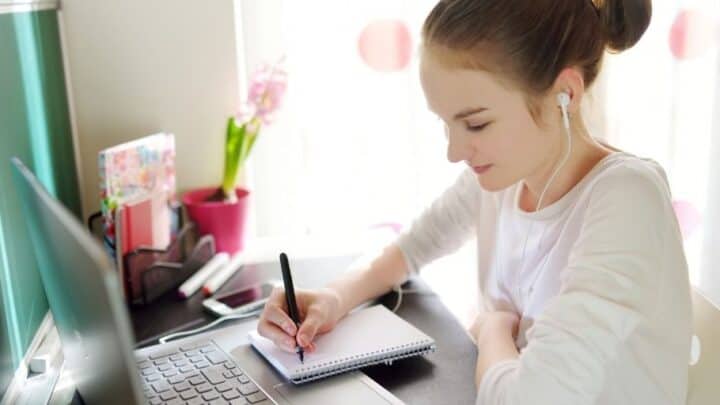 18 year old girl with headphones in at desk, working on budget