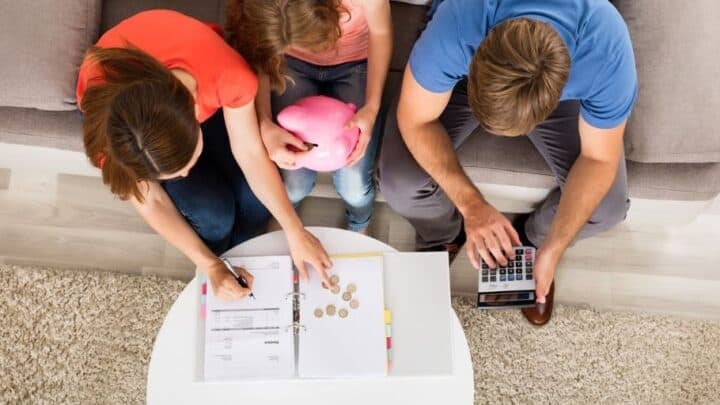 young teen girl with mom and dad working on money management skills with calculator and piggy bank at coffee table