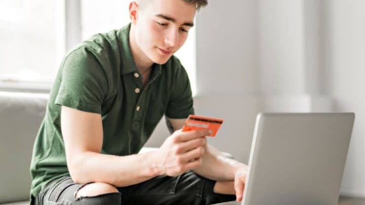 teen boy with orange credit card at laptop, smiling