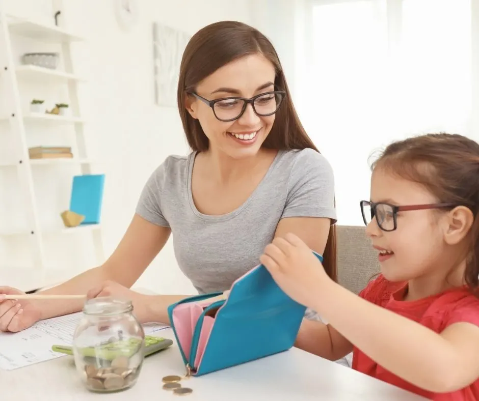 mother with preschool daughter, both smiling, playing with a wallet and calculator while educating child on money