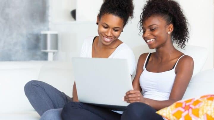 teen with mother, sitting on couch with laptop smiling, working on how to budget as a teenager