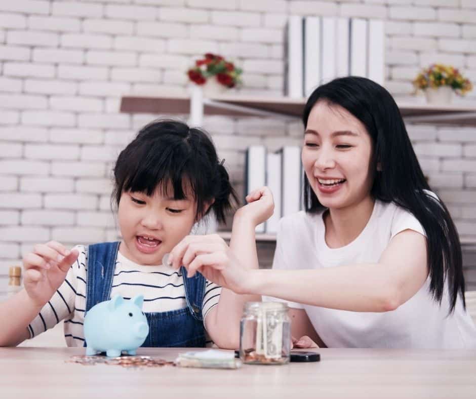 mother helping preschool daughter count coins in her blue piggybank, both having fun learning about money concepts