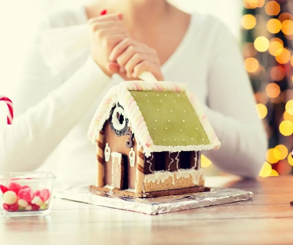 teen decorating gingerbread house with green roof, black sides, and white frosting