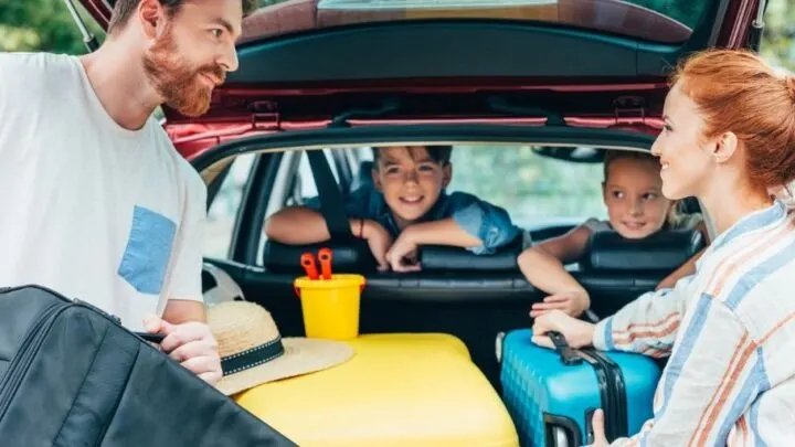 parents packing up trunk with two kids looking on, readying to survive a family road trip