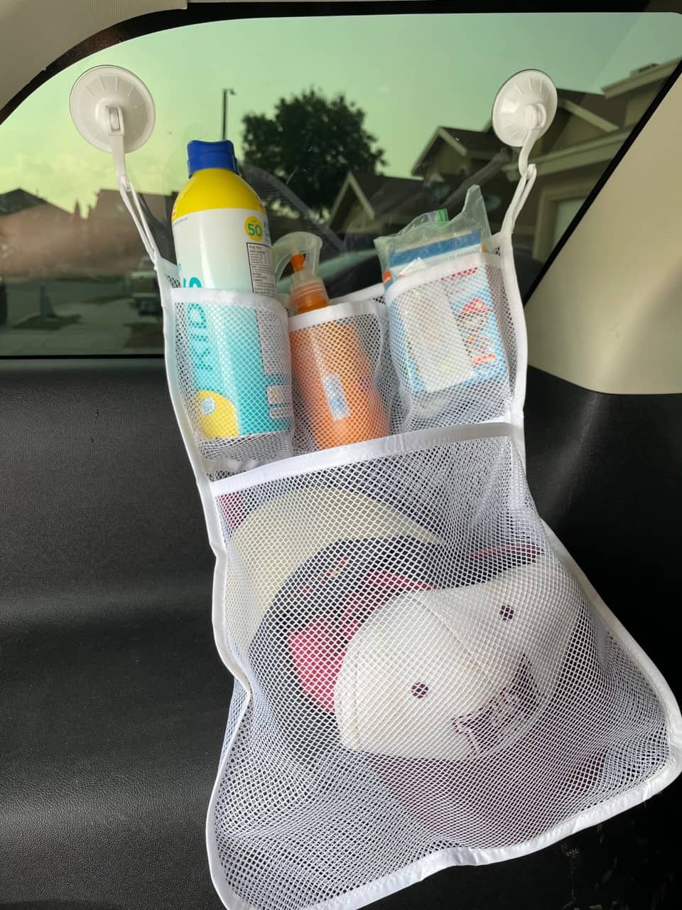 mesh bath toy organizer with sunscreen and hats in window in trunk of car