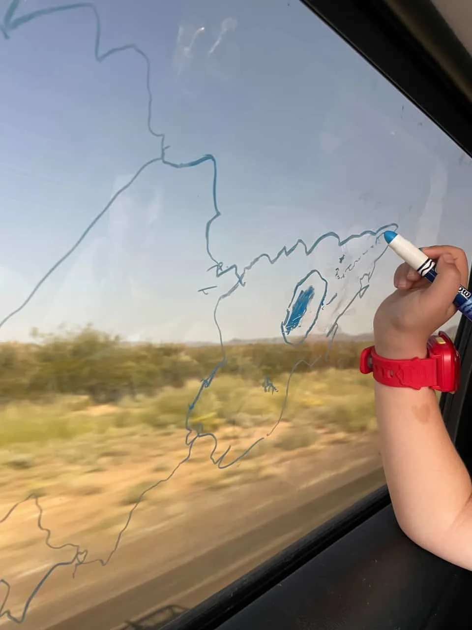 hand of 4-year-old drawing on window with window paint markers