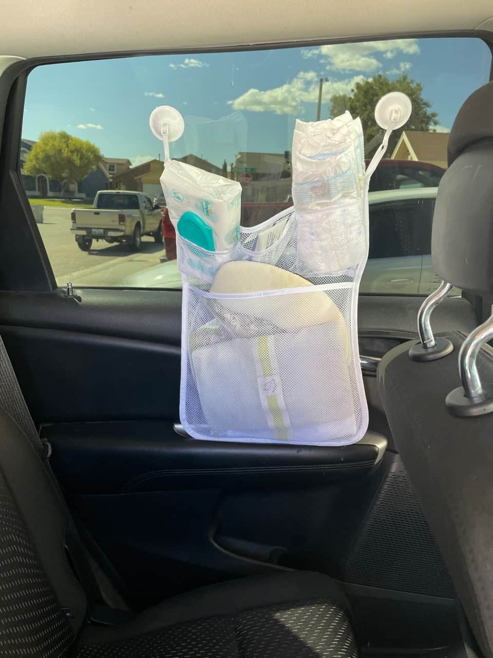 mesh bath toy organizer on inside car window, with baby wipes, changing pad, diapers and ointment