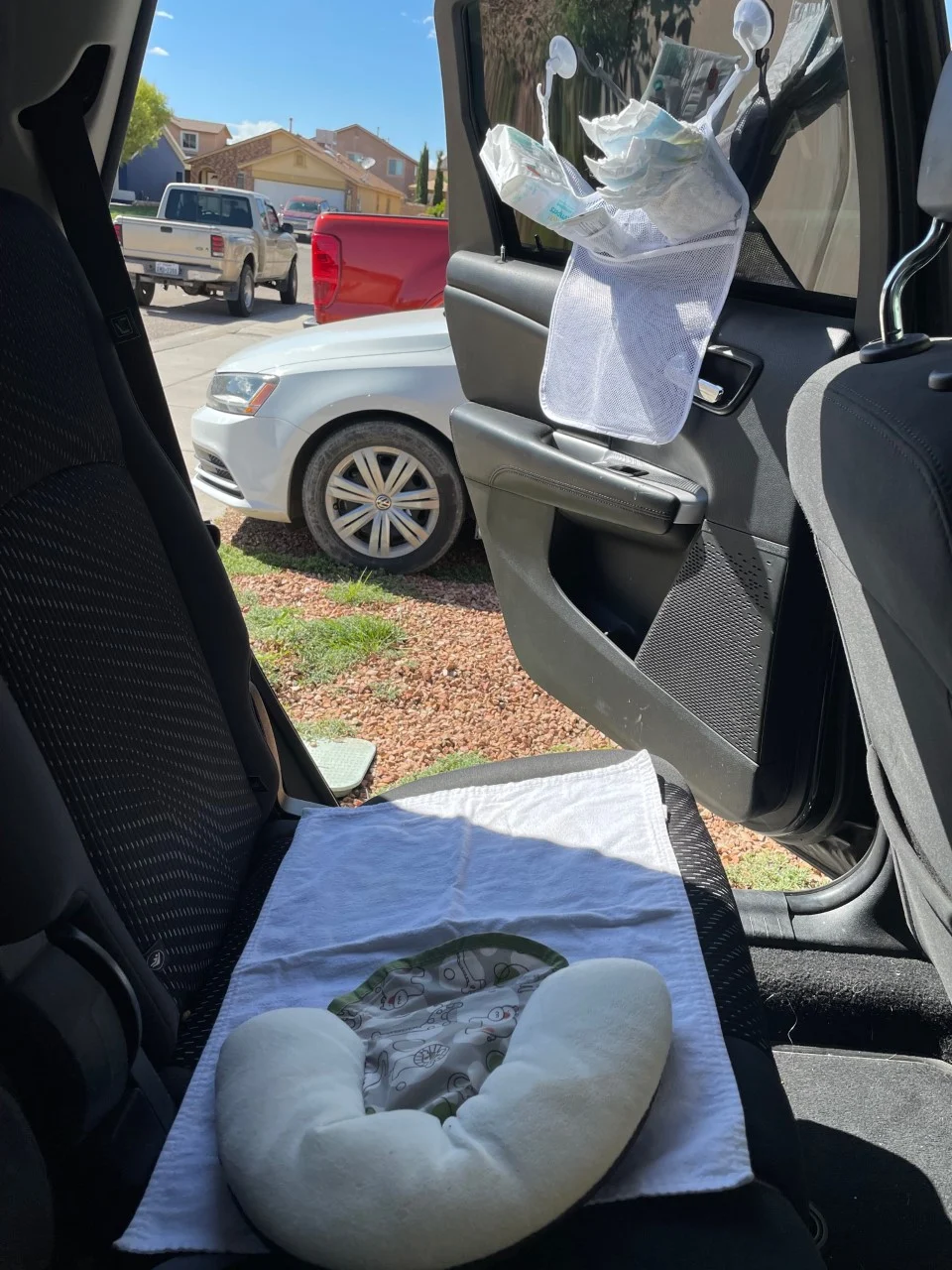 diaper changing station setup on seat and with mesh bath toy organizer on inside car window, filled with baby wipes, diapers, ointment, etc. 