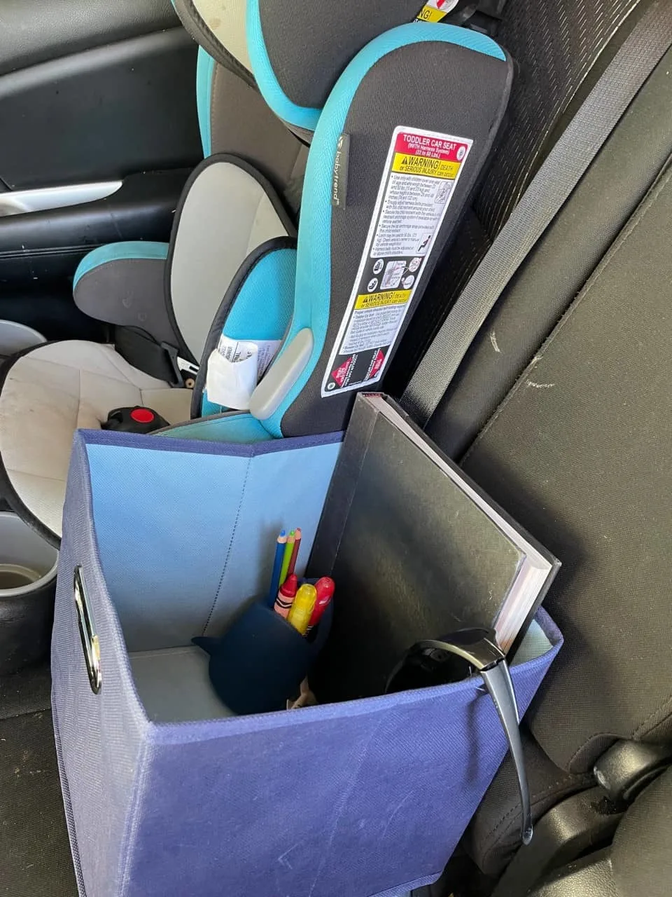 cloth bin next to child seat with sunglasses, rubber shark toothbrush holder with window paint markers and crayons, and book