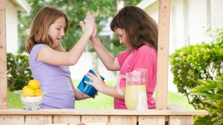 two kids slapping each other five, looking in money jar at lemonade stand