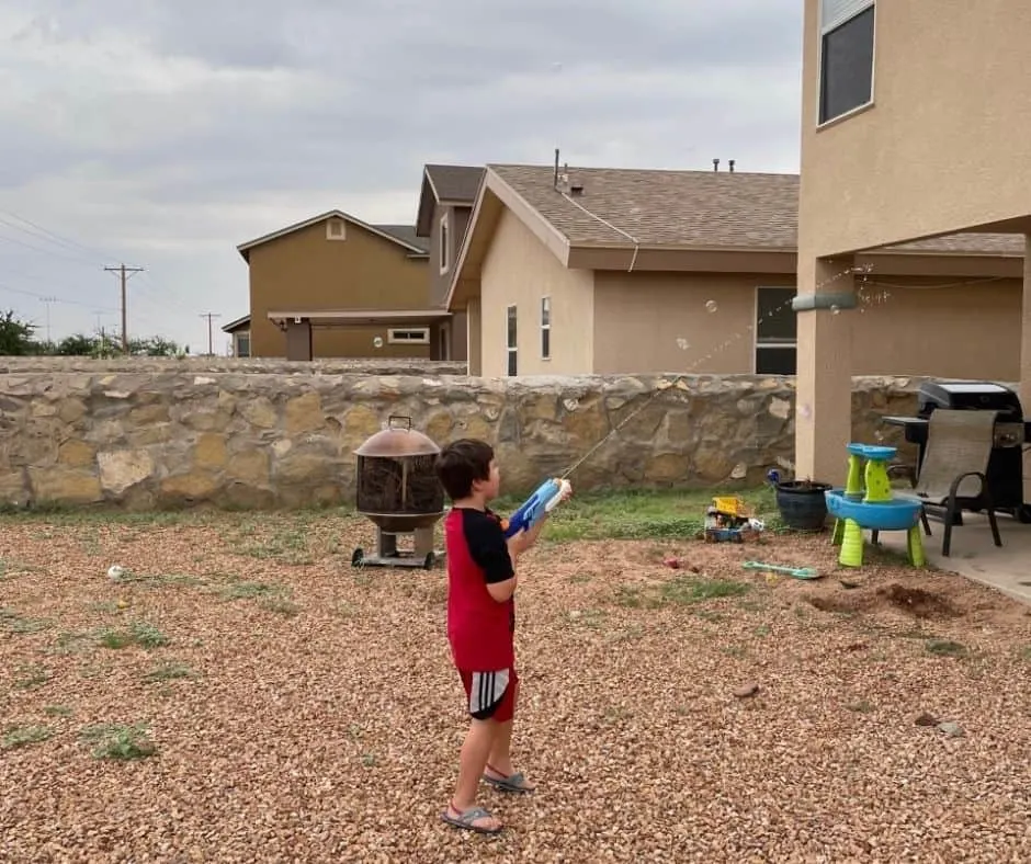 5 year old using a water gun to spray down bubbles floating in the air