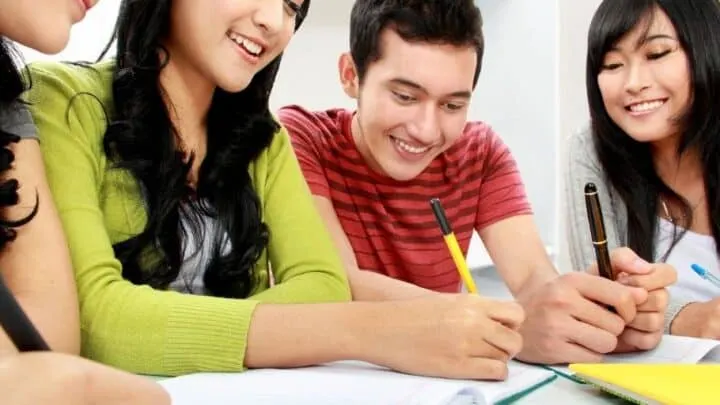 group of high school students working on budget project at a table, smiling