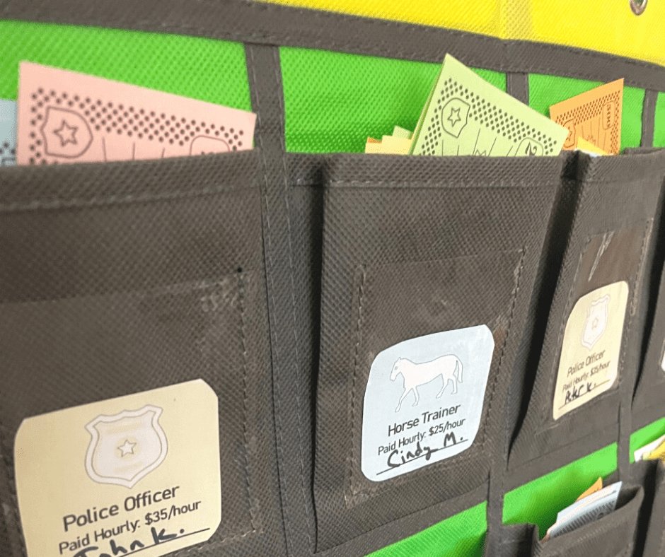 green and black pocket chart with pretend money on inside, student name and job token on outside