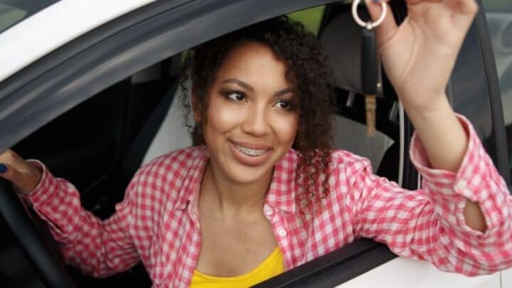 teen girl holding keys, smiling, in driver's seat of car