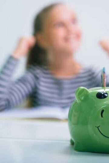 girl celebrating saving money, with green piggy bank in the forefront