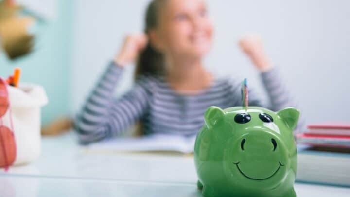 girl celebrating saving money, with green piggy bank in the forefront