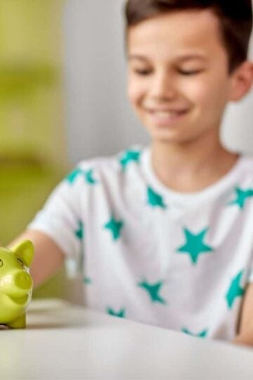 boy in a teal star shirt, putting money into funky green piggy bank and smiling