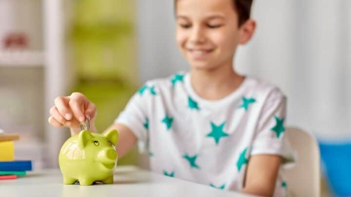 boy in a teal star shirt, putting money into funky green piggy bank and smiling