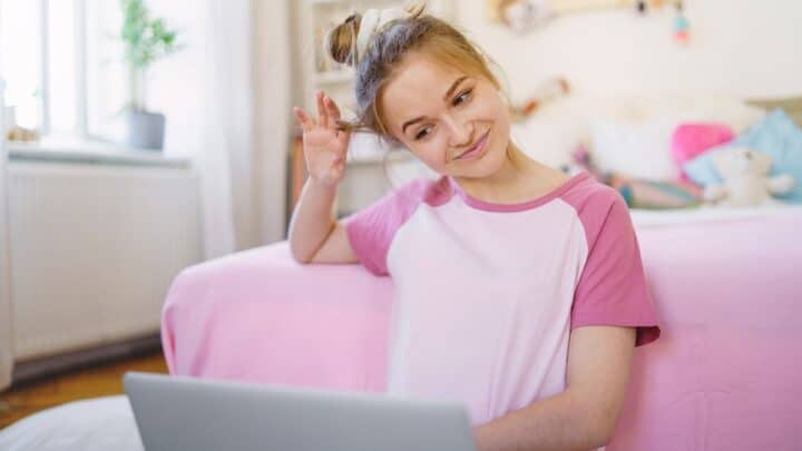 teen girl in pink shirt, weighing pros and cons of having a job as a teenager looking at her laptop