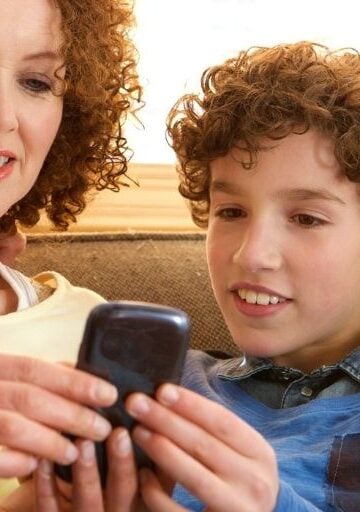 mother and son looking at busykid prepaid debit card app on phone, on couch