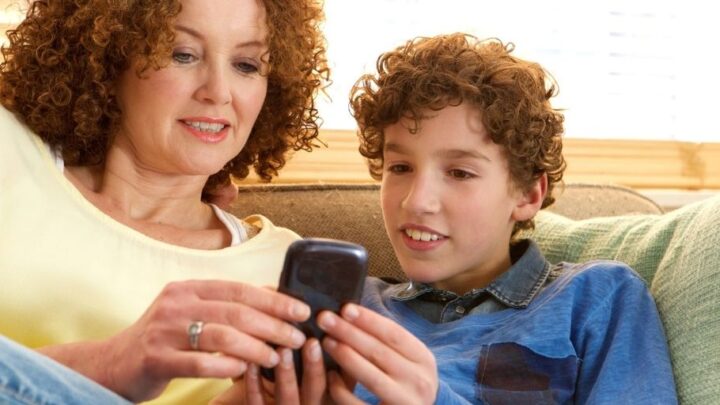 mother and son looking at busykid prepaid debit card app on phone, on couch